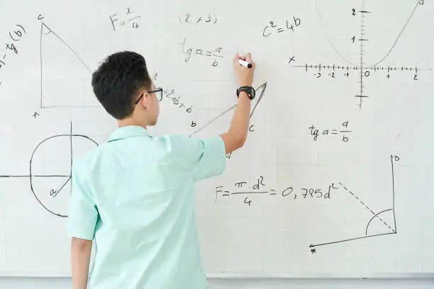 Schoolboy in glass writing geometry equation on whiteboard, view from the back