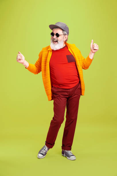 Senior hipster man wearing eyeglasses posing on green background. Tech and joyful elderly lifestyle concept