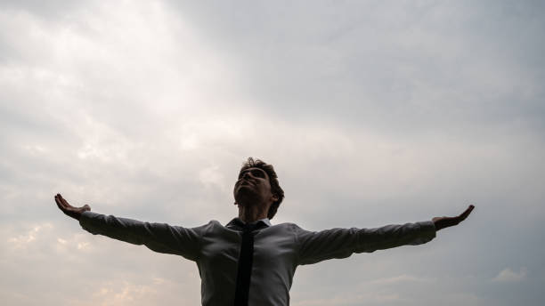 istock Young businessman standing under cloudy grey sky aith his arms spread widely 1269810855