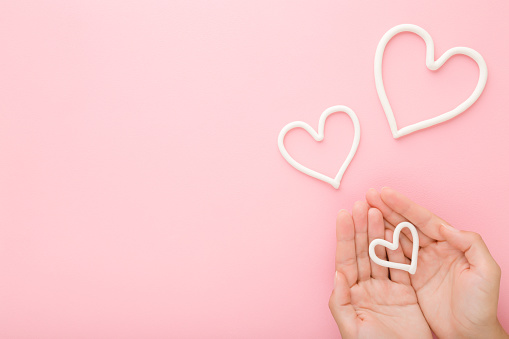 Young woman palms and white heart shapes on light pastel pink table background. Love and happiness or care about hands skin concept. Empty place for inspirational text, quote or sayings. Top view.