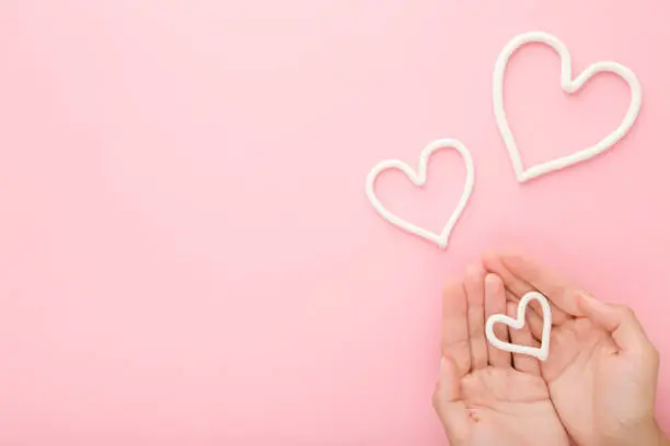 Photo of Young woman palms and white heart shapes on light pastel pink table background. Love and happiness or care about hands skin concept. Empty place for inspirational text, quote or sayings. Top view.