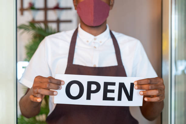 istock Hands of waiter in uniform and protective mask holding paper with notice open 1269814549