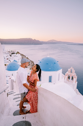 Santorini Greece, young couple on luxury vacation at the Island of Santorini watching sunrise by the blue dome church and whitewashed village of Oia Santorini Greece . Europe