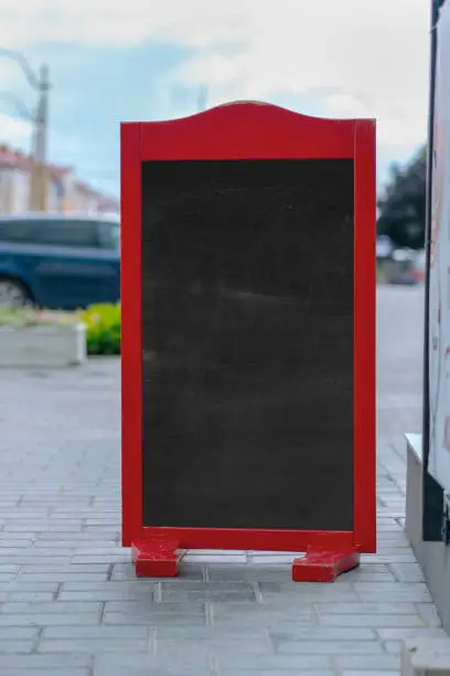 vertical empty chalkboard for menu in wooden red frame on street sidewalk near cafe entrance outside