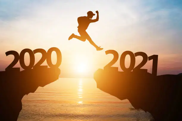 Photo of Silhouette man jump from 2020 to 2021 on cliff with sunlight for change and welcome the new year.