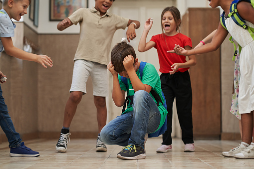 Mischief students bullying thier classmate, pointing on him, laugh at him and make him sad