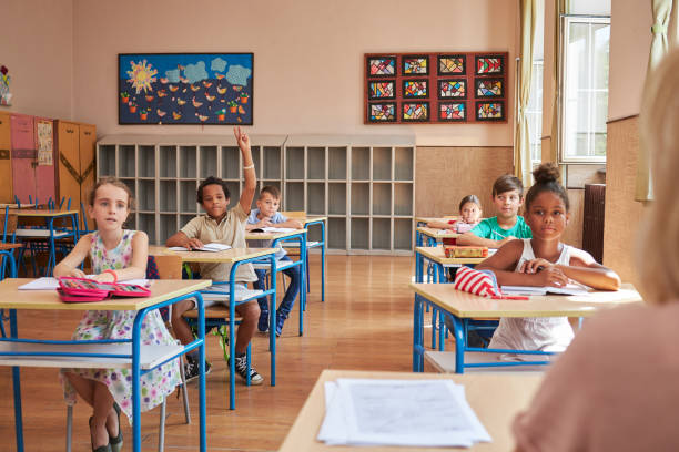 istock Smart diverse schoolboy raising his hand so he can give the answer to teacher question 1269827098