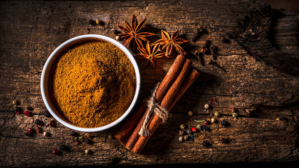 Scented spices background: Cinnamon powder, cinnamon sticks, star anise and cloves Scented spices background: top view of a white bowl filled with cinnamon powder shot on rustic wooden table. Cinnamon sticks, star anise, cloves and peppercorns are all around the bowl.  Predominant color is brown. The composition is at the left of an horizontal frame leaving useful copy space for text and/or logo at the right. High resolution 16:9 format studio digital capture taken with SONY A7rII and Zeiss Batis 40mm F2.0 CF lens Cinnamon stock pictures, royalty-free photos & images