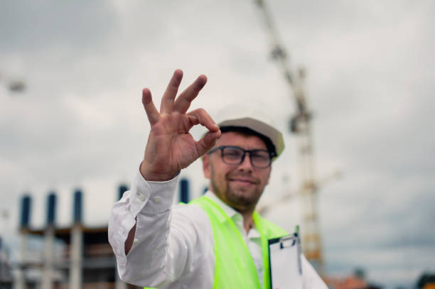 istock Chief in a vest and a construction helmet with documents in his hands, against the background of a tower crane and the sky with clouds. House construction inspection. 1269840284