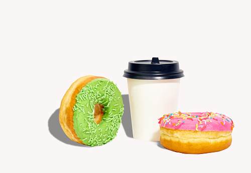 Sweet glazed donuts and a coffee cup isolated on pink background with copy space. Junk food breakfast