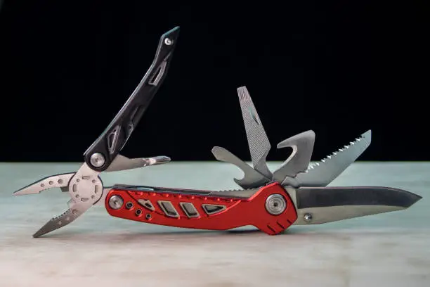 Beautifil red-black multitool on white surface. Black background.