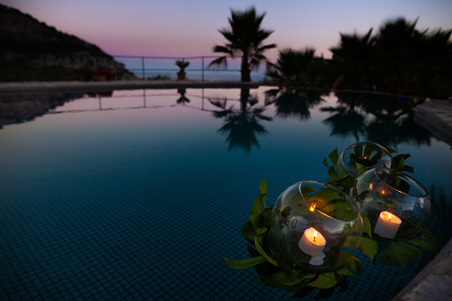 Candle glasses swimming in the swimming pool at sunset