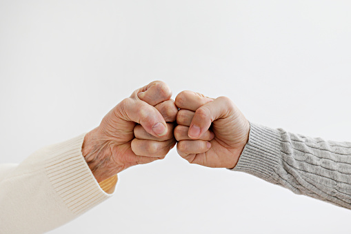 Two women of different age fist bumping over white wall background. Grandmother bonding with her granddaughter. Close up, copy space for text, isolated.
