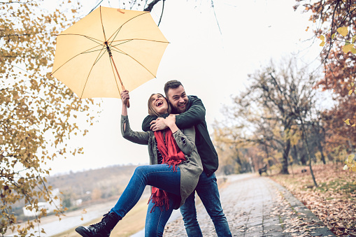 Couple Embracing And Holding Umbrella In Park