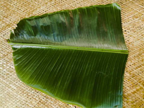 Banana leaf for Onam sadhya placed on a mat.The leaf is long and with green color.The leaf has lines on it to either sides from the center line.