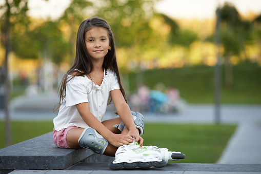 happy little child girl in roller skates is sitting in summer park.