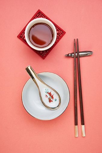 chise table setting of rice bowl spoon and chopsticks on red background