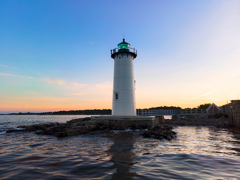 Iconic New England style white and black lighthouse on New Hampshire coast at sunset against vivid blue and orange sky.