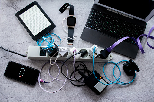 Many gadgets - smartphone, wireless headphones, laptop, smart watch, camera battery and e-book are charged on one power strip