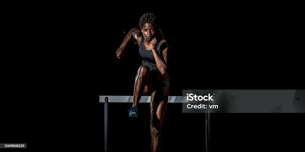 African-American woman running away from a hurdle Front view of an African-American female athlete running away from a hurdle towards the camera. Athlete Stock Photo