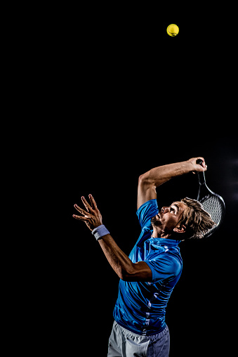 Vertical photo of a caucasian male tennis player serving the ball on black background.