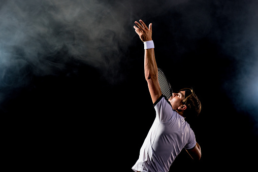 Male caucasian tennis player serving on a black background.