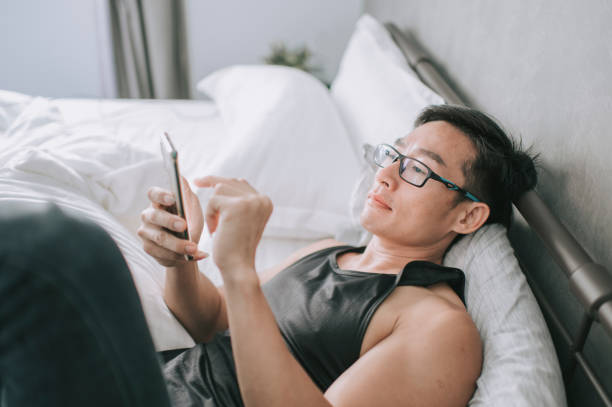 istock asian chinese handsome man lying down on bed checking phone message browse internet with his smart phone 1269860181