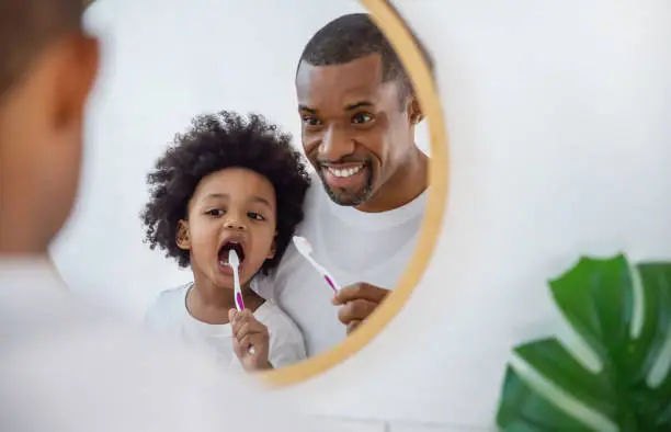 Photo of Portrait of happy family black African American father and son child boy brushing teeth in the bathroom. Morning routine with toothbrushes, fatherâs day concept