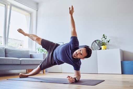 Athletic man doing side plank star during workout at home