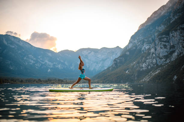 tranquil scene of woman doing warrior i pose on paddleboard - lake bohinj imagens e fotografias de stock