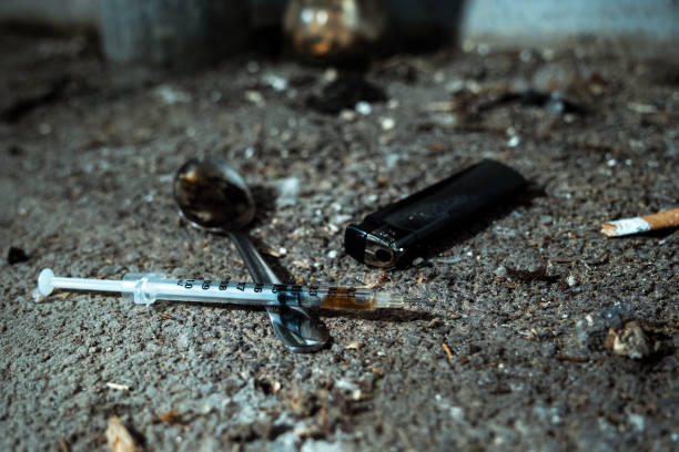 Night shoot of a dirty spoon with used heroin, a lighter and a syringe on a floor. Symbol for drug addiction and substance abuse. Addiction to opioids. Junkie leaves trash. evidence photos stock pictures, royalty-free photos & images