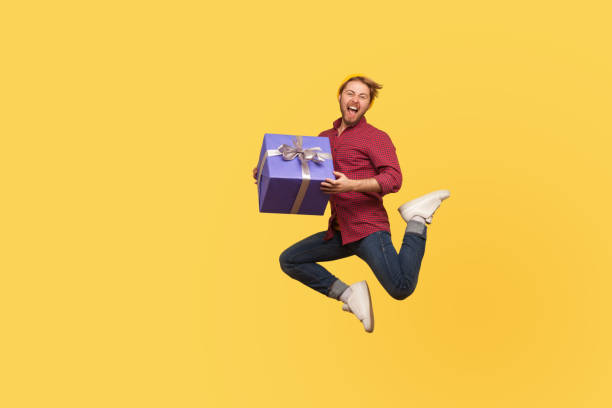 istock Enthusiastic extremely joyful hipster guy jumping trampoline with gift box, flying in air holding birthday present 1269869837