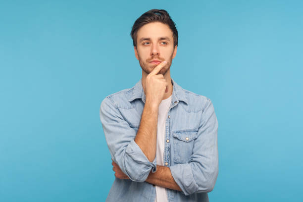 hmm, réfléchissons ! verticale de l’homme beau pensif dans la chemise de denim de travailleur touchant le menton tout en réfléchissant le plan - curiosité photos et images de collection