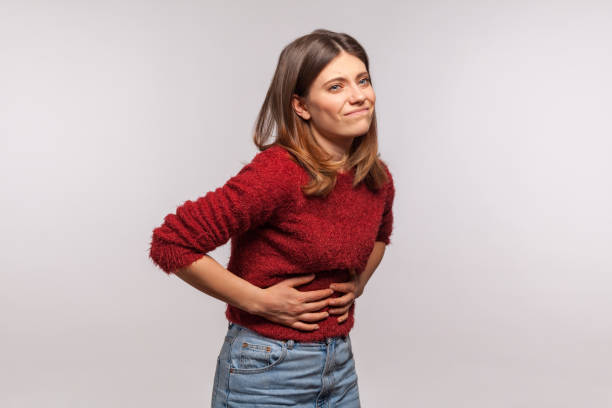 Girl touching belly, grimacing from stomach ache, severe abdominal distress, symptoms of constipation Girl in shaggy sweater touching belly, grimacing from stomach ache, severe abdominal distress, symptoms of constipation, indigestion, gastrointestinal disorder. studio shot isolated on gray background heartburn photos stock pictures, royalty-free photos & images