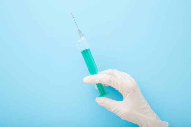 istock Doctor hand in white rubber protective glove holding syringe on light blue table background. Pastel color. Healthcare concept. Closeup. Top down view. 1269879798