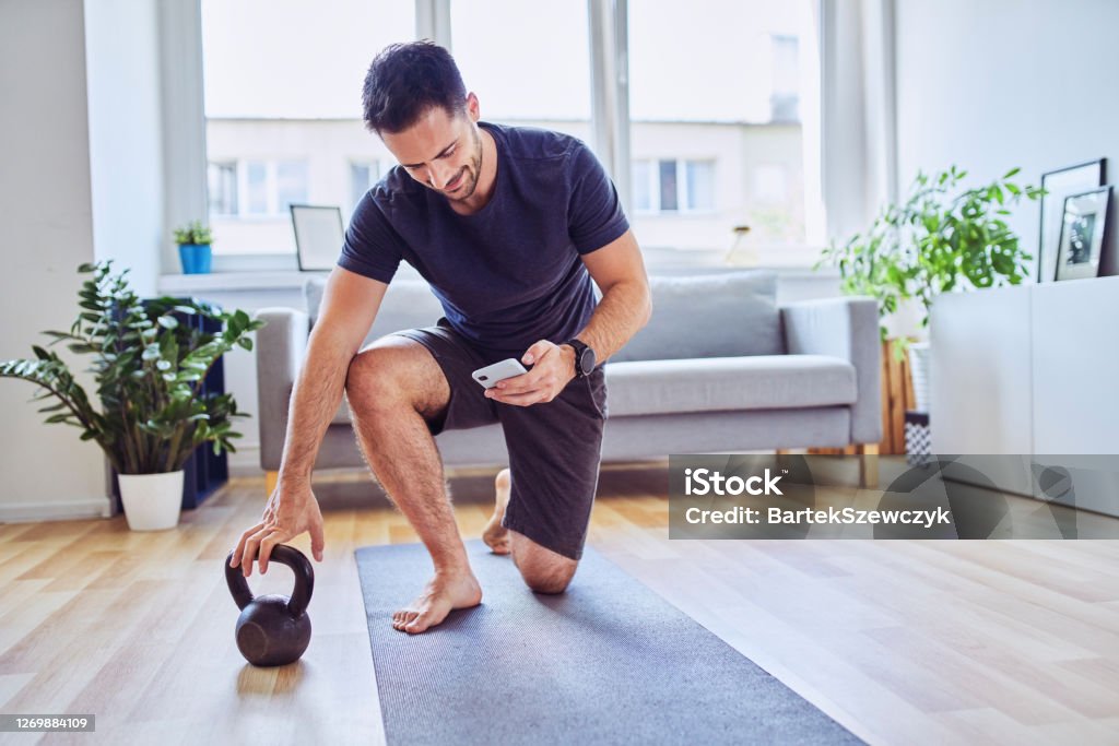 Man with smartphone checking training app before home workout exercises Exercising Stock Photo