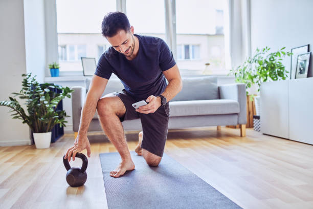 man with smartphone checking training app before home workout exercises - kettle bell exercising healthy lifestyle sports clothing imagens e fotografias de stock
