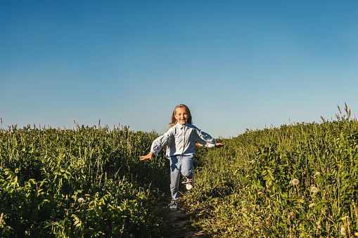 Happy girl run in field. Blue sky, green meadow. Girl lose two baby teeth.