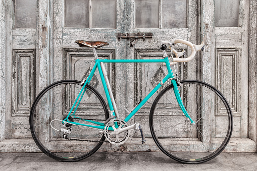 Vintage seventies light blue racing bicycle with leather saddle in front of old black and white wooden doors