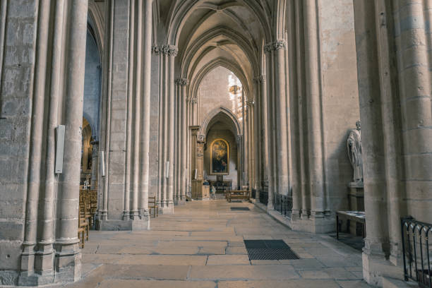 A dramatic interior view of the Cathedral of St. Michael and St. Gudula in Brussels, Belgium. The towering Gothic columns and ribbed vaults lead the eye toward the altar. Statues of saints adorn the massive pillars, with one notably holding a golden sword, contrasting with the dark, moody lighting of the cathedral.