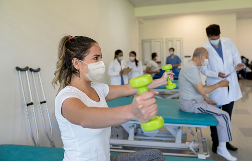 Portrait of a Latin American woman using weights while doing physiotherapy and wearing a facemask during the COVID-19 pandemic â healthcare and medicine concepts