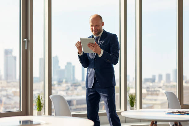 istock Elegant businessman holding a document folder standing near window in office. 1269899762