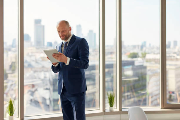 istock Elegant businessman holding a document folder standing near window in office. 1269899767