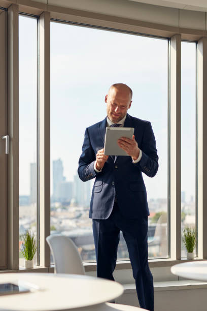 istock Elegant businessman holding a document folder standing near window in office. 1269899778