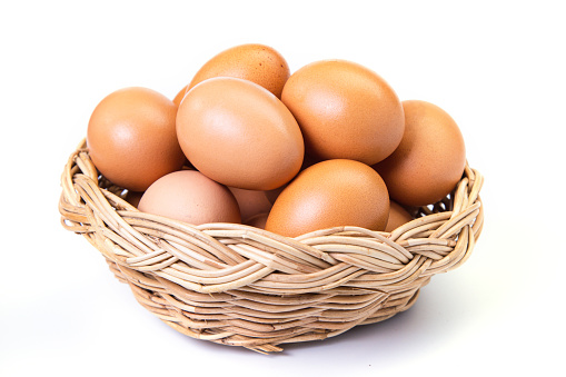 Eggs in basket on white background. Brown eggs in a wicker basket on white background.