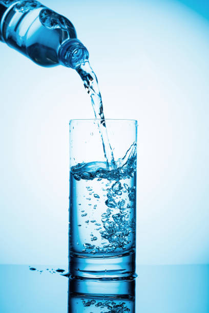 istock Pouring water from a bottle into glass on a blue background. 1269902146
