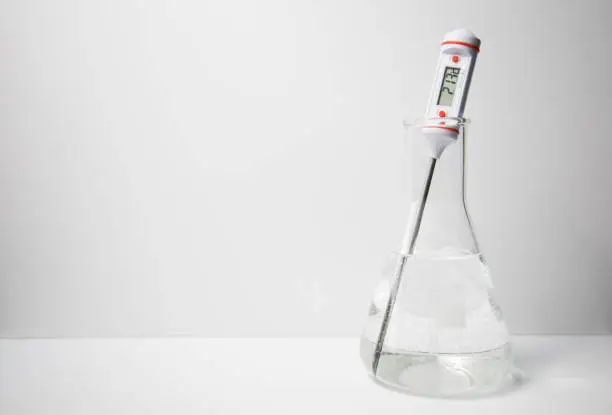 A digital thermometer measuring the temperature of a liquid in a glass erlenmeyer flask on a white background. Science experiment. Temperature measuring.