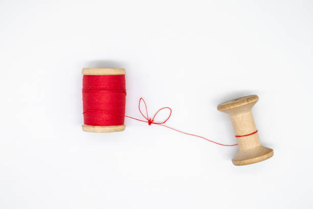 Two wooden spools of thread. One is full, the other almost empty, connected by a single thread with a knot in the shape of a heart. Love and togetherness as a concept, without people Two wooden spools of thread. One is full, the other almost empty, connected by a single thread with a knot in the shape of a heart. Love and togetherness as a concept, without people wooden spool stock pictures, royalty-free photos & images