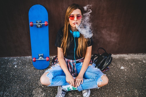 Young skateboarder woman smoking smoking marijuana joint outdoors