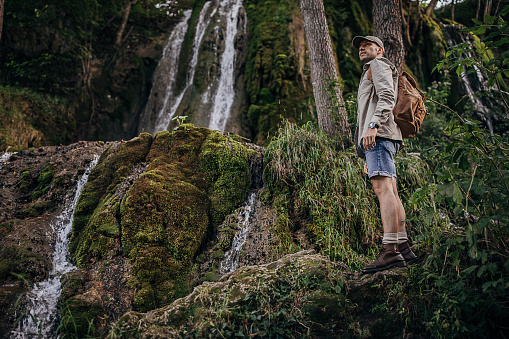 One man, male hiking alone in nature, he is standing by the waterfall.